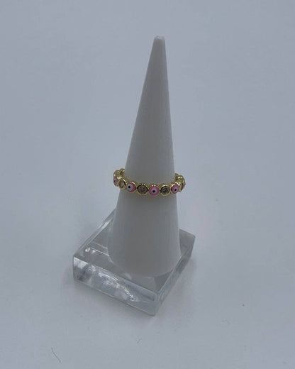 Gold ring with pink stones on a white cone-shaped stand against a light gray background