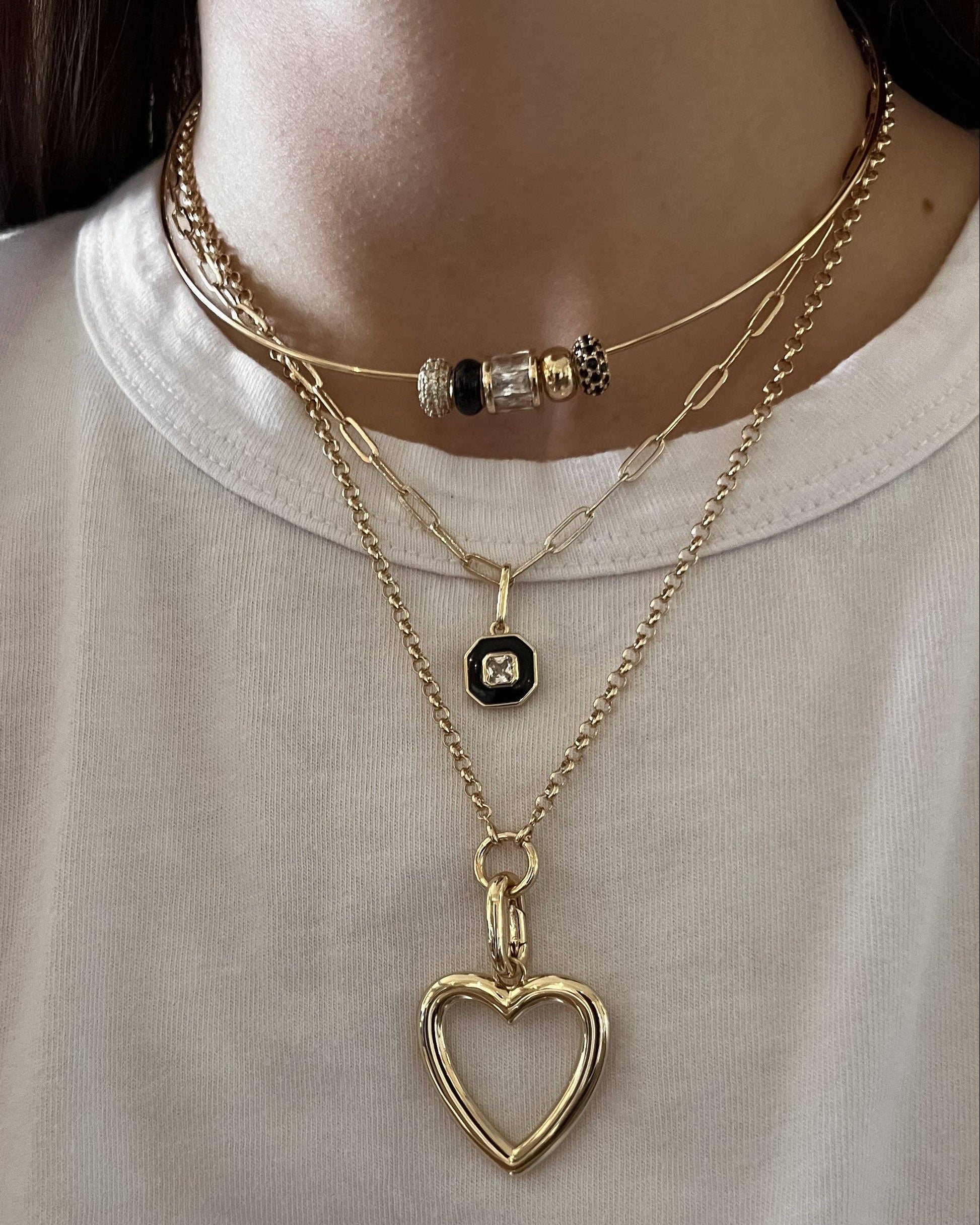 Person wearing multiple gold necklaces with heart pendants on a plain background