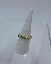 Gold ring with green gemstones on a white stand against a light gray background