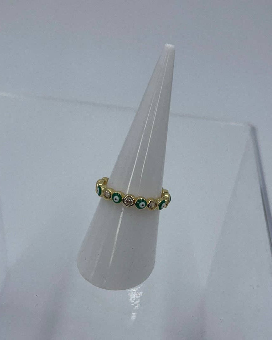 Gold ring with green gemstones on a white stand against a light gray background