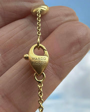 Gold earring with 'Marco Bicego' logo held in a hand against a blurred natural background