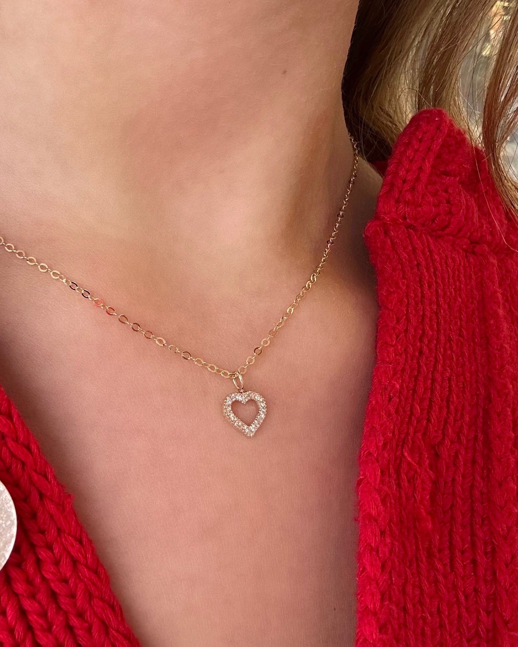 Close-up of a person wearing a red knitted garment with a heart-shaped pendant necklace.