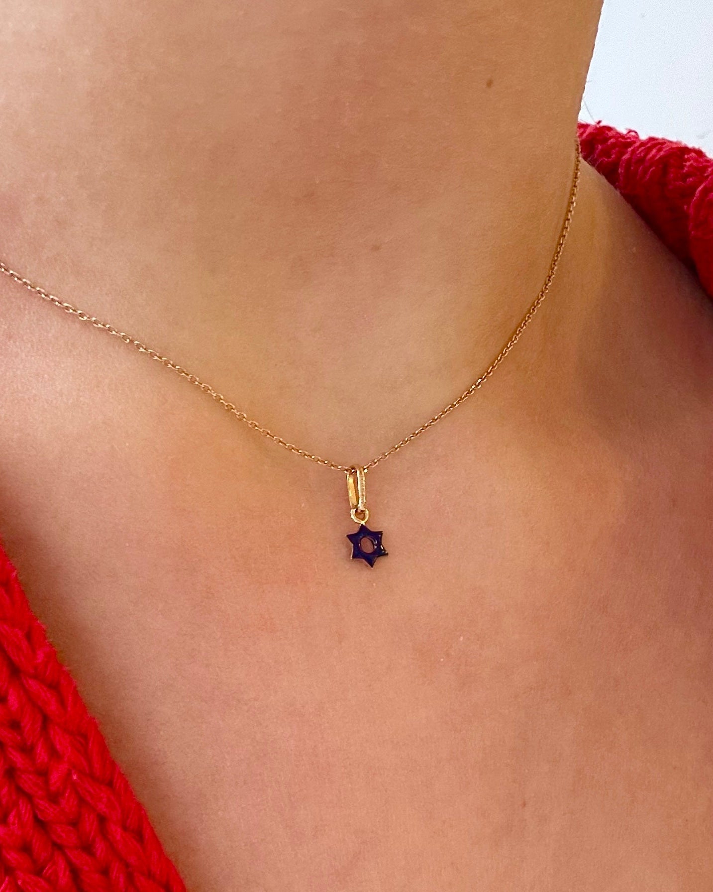 Gold necklace with a purple gemstone pendant on a person wearing a red garment.