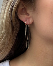 Close-up of a person wearing the Métier By Tomfoolery Double Add-on Chain by Métier by Tomfoolery, featuring double hoop earrings joined by two gold chains—the ideal Hoop Earring Add-On for a stylish layered look.
