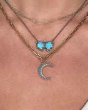 The DYLANJAMES BLAIR Butterfly Necklace features layered elegance: a thin gold chain with turquoise accents, a silver butterfly necklace with blue pendant, and a gold chain with blue crescent moon pendant—all beautifully worn together.