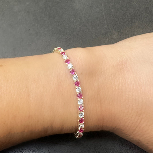 The GEORGE Tennis Bracelet by Dylan James Jewelry features a luxurious gold-plated design with alternating pink and clear cubic zirconia gemstones that beautifully adorn the wrist.