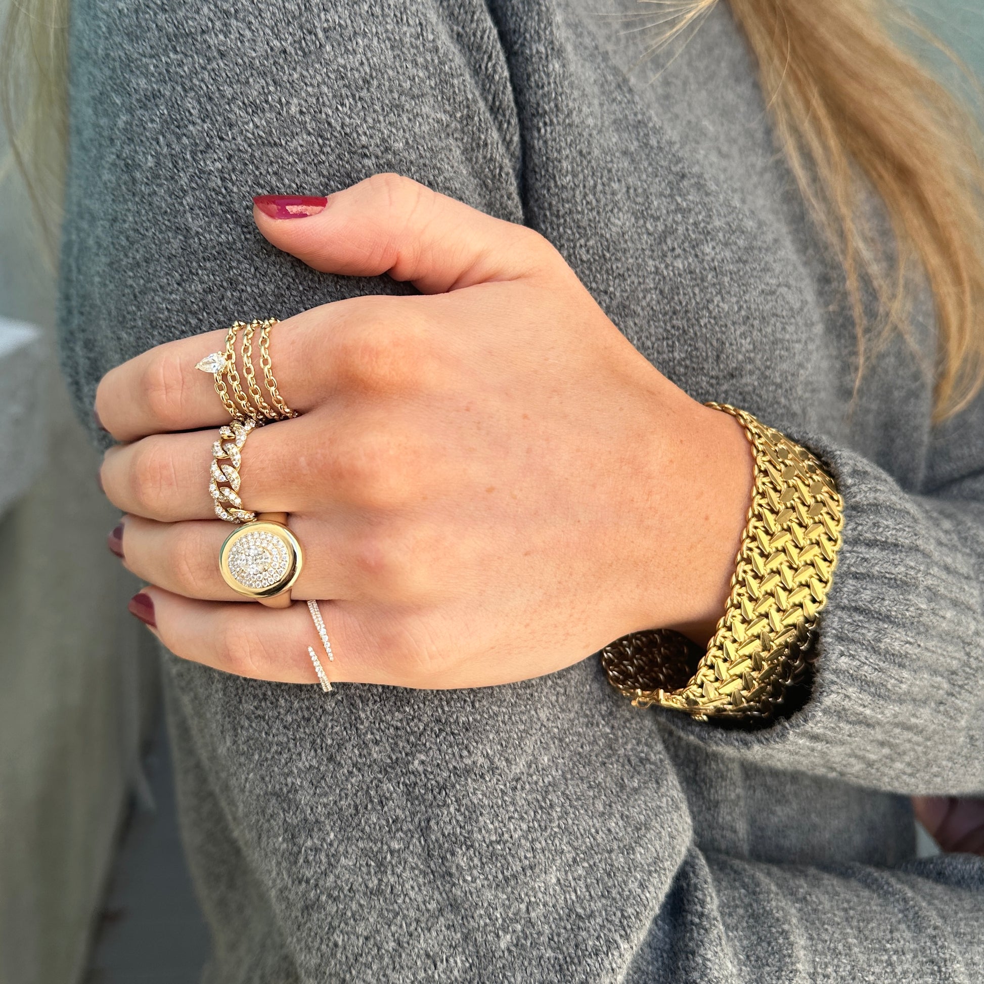 A person wearing multiple yellow gold rings, featuring the AIRA LEE Gold Diamond Ring with a pear-shaped diamond in size 7, and bracelets on their left hand and wrist, displayed against a gray sweater.