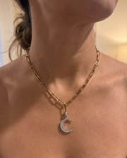 A close-up of a model's neck and upper chest wearing a gold chain necklace with a crescent moon pendant. The pendant is adorned with small clear stones.