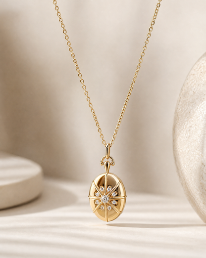 A gold pendant necklace featuring a compass rose design with a central cluster of small clear stones, displayed on a soft beige surface with a textured ceramic object in the background.