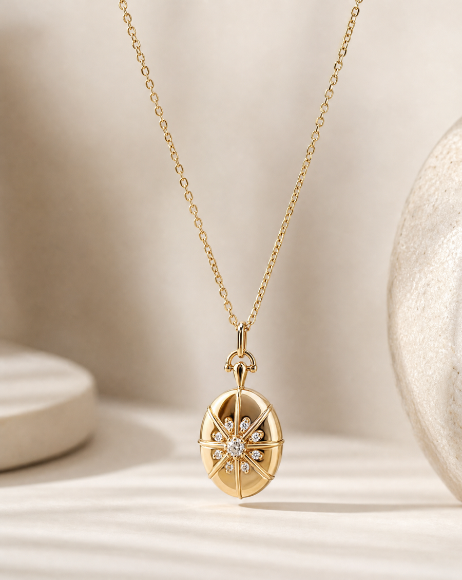 A gold pendant necklace featuring a compass rose design with a central cluster of small clear stones, displayed on a soft beige surface with a textured ceramic object in the background.
