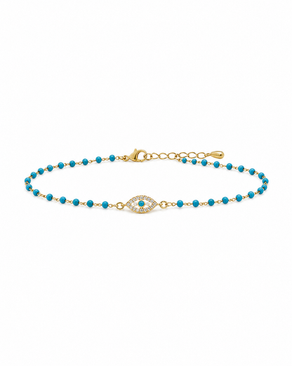 A delicate gold chain bracelet featuring small turquoise blue beads and a central gold evil eye charm with a turquoise center, displayed on a clean white background.