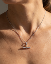 A close-up of a model's neck and chest wearing a delicate silver chain necklace with a toggle clasp pendant. The toggle bar is set with small clear stones, and the center of the toggle features a small gold accent.