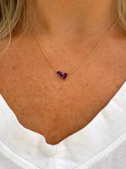 A woman wearing the AIRA BARNEY Amethyst Necklace—an adjustable 14kt yellow gold piece featuring two purple gemstones—seen close-up against her neck and white shirt.