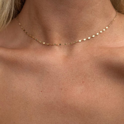 The LIV Gold Chain from Dylan James Jewelry graces the neck with its 14kt yellow gold and small leaf-shaped charms, its delicate diamond cut chain shimmering softly. This elegant piece measures 16 inches in length, set against a neutral backdrop.