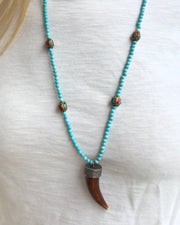 The JOE turquoise Beaded Necklace by Dylan James Jewelry features red and green inlay accent beads and a bold horn-shaped pendant, perfect for styling over a white shirt.