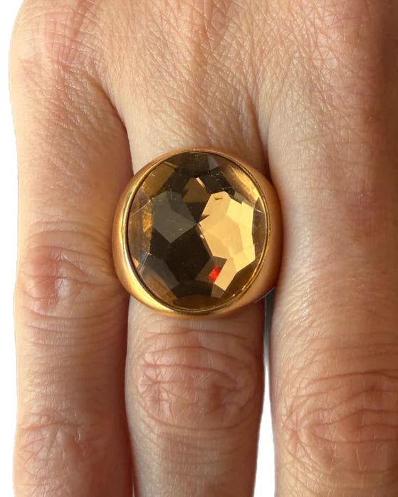 Gold ring with a large gemstone on a hand against a white background