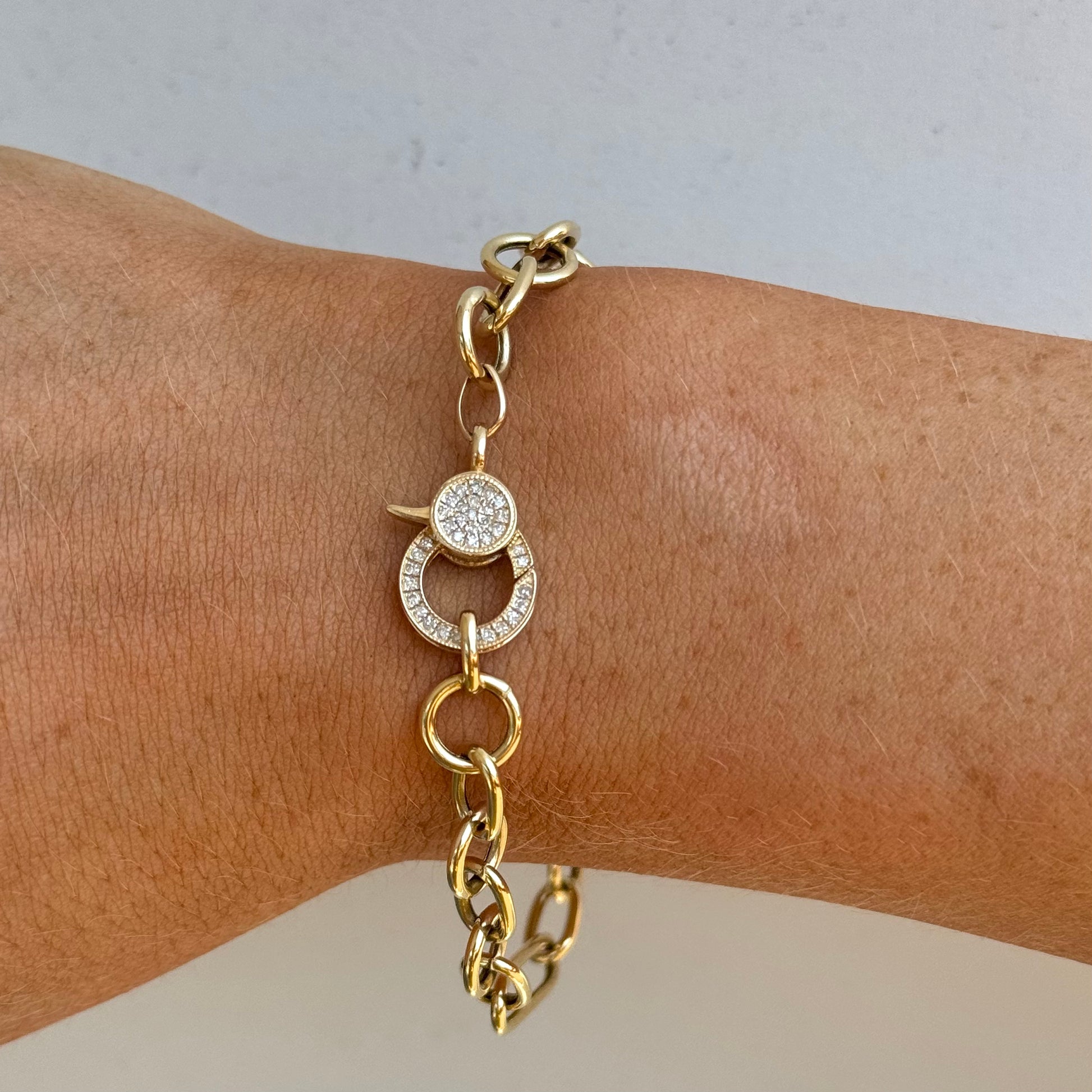 The WILLAM Gold Diamond Bracelet by Dylan James Jewelry elegantly adorns a wrist against a light background, featuring 14kt yellow gold, a circular diamond closure, and sparkling embellishments.