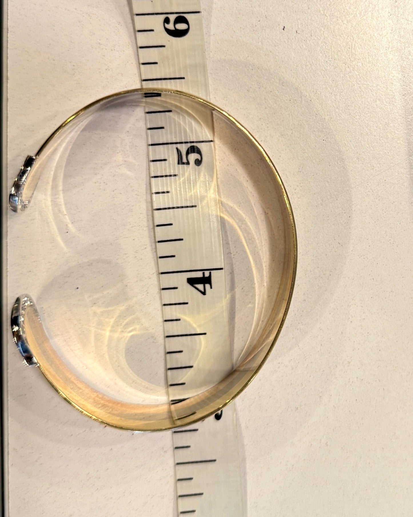 Gold bracelet being measured with a tape measure on a white background