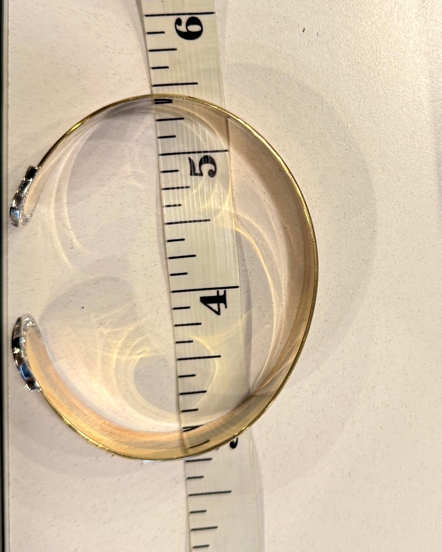 Gold bracelet being measured with a tape measure on a white background