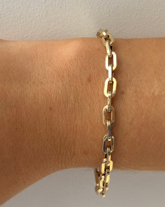 Gold chain bracelet on a wrist against a neutral background