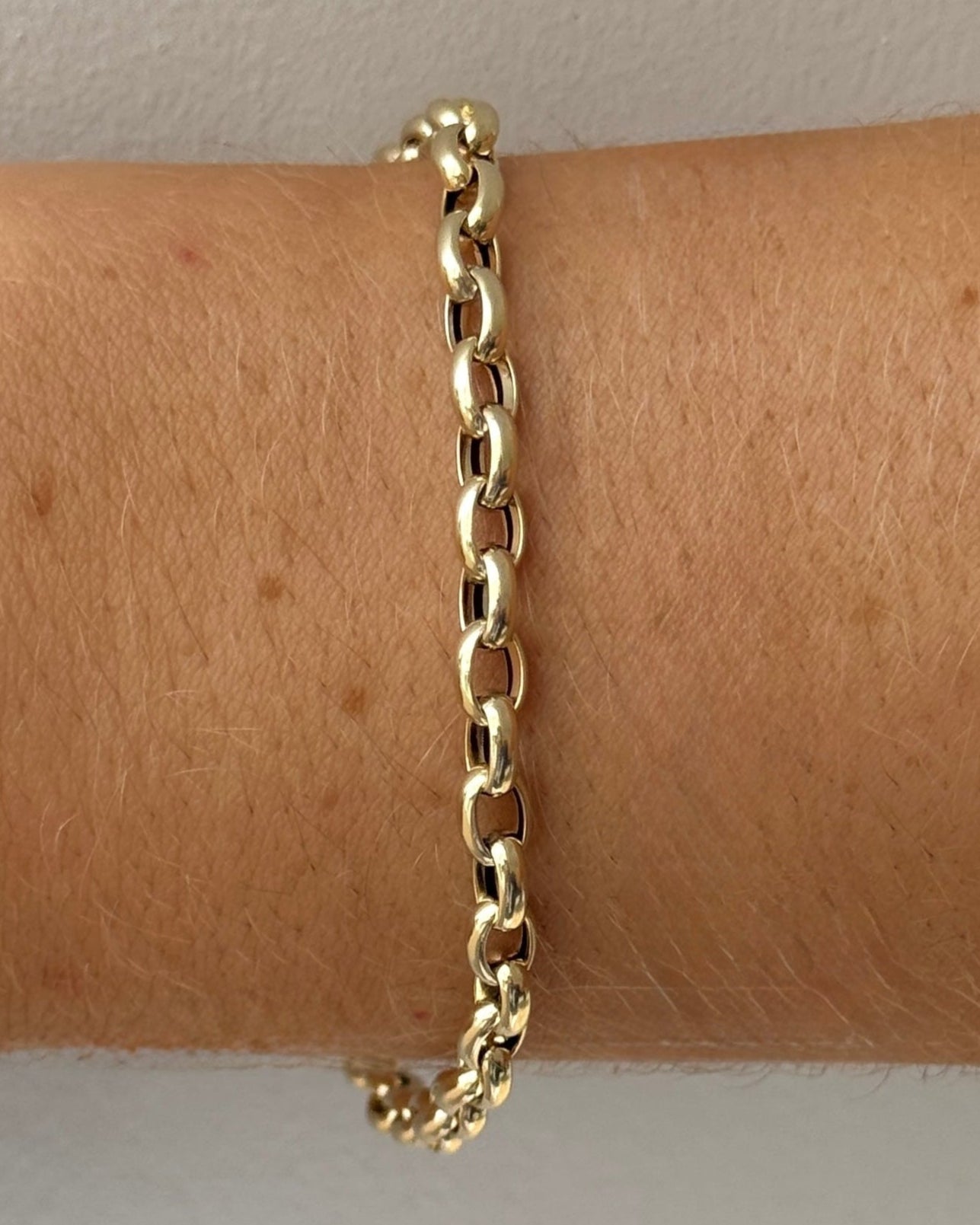 Gold chain bracelet on a wrist with a plain background