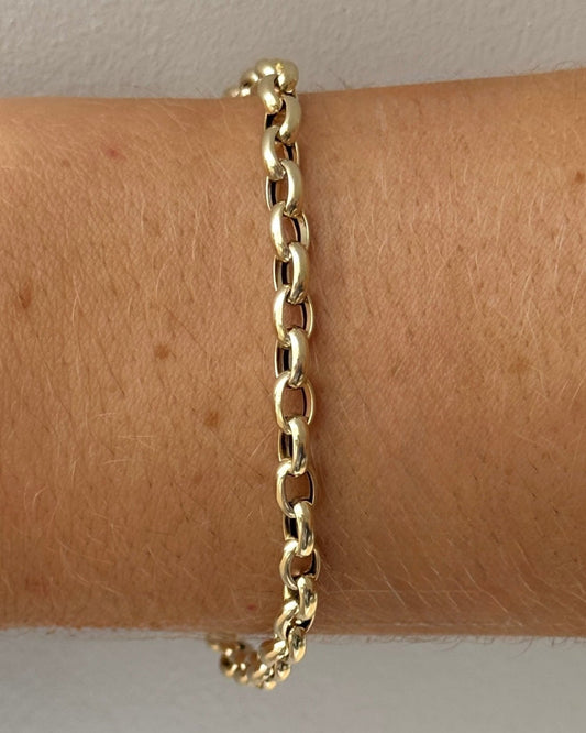 Gold chain bracelet on a wrist with a plain background