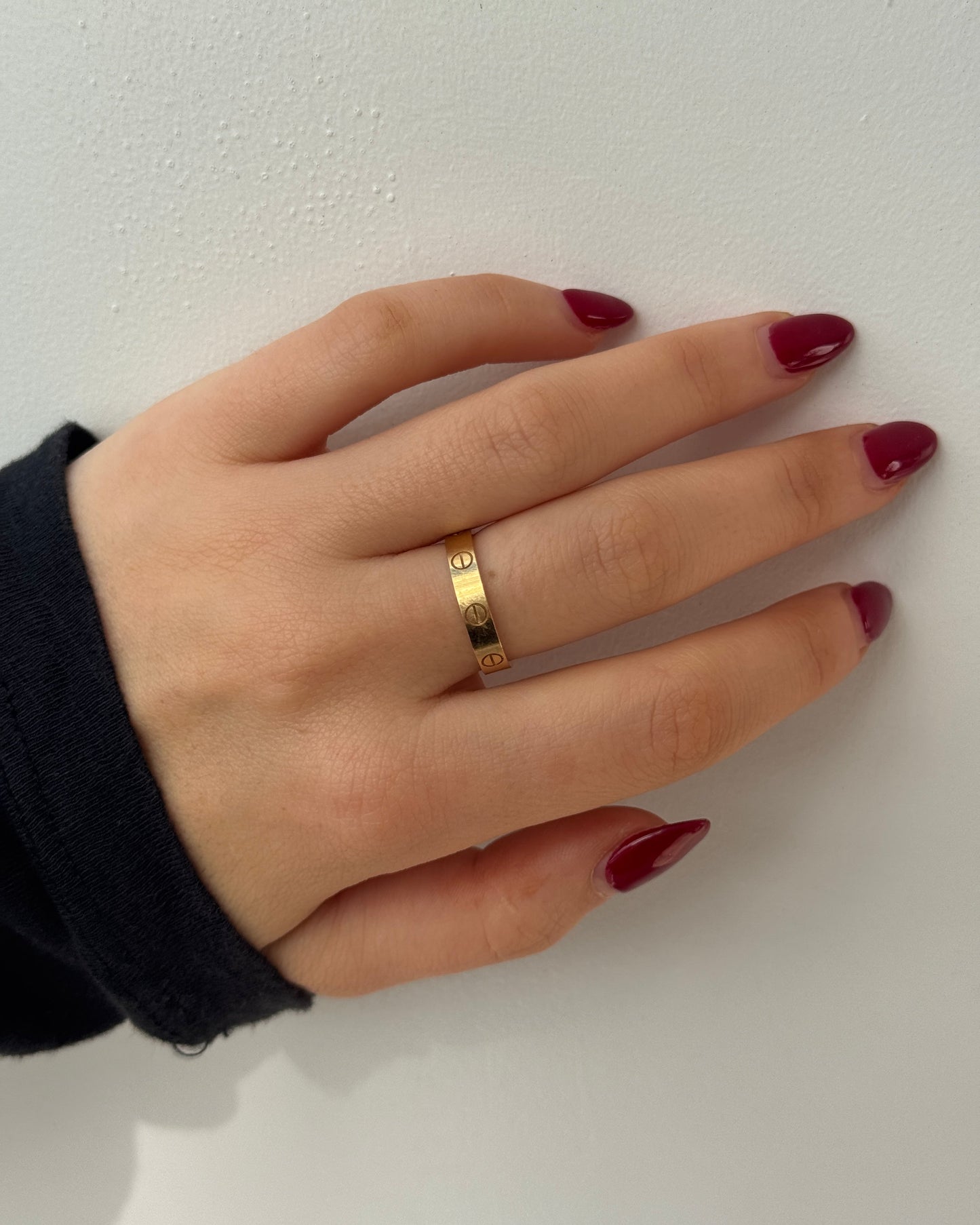 Hand wearing a gold cartier love ring with red nail polish on a white background