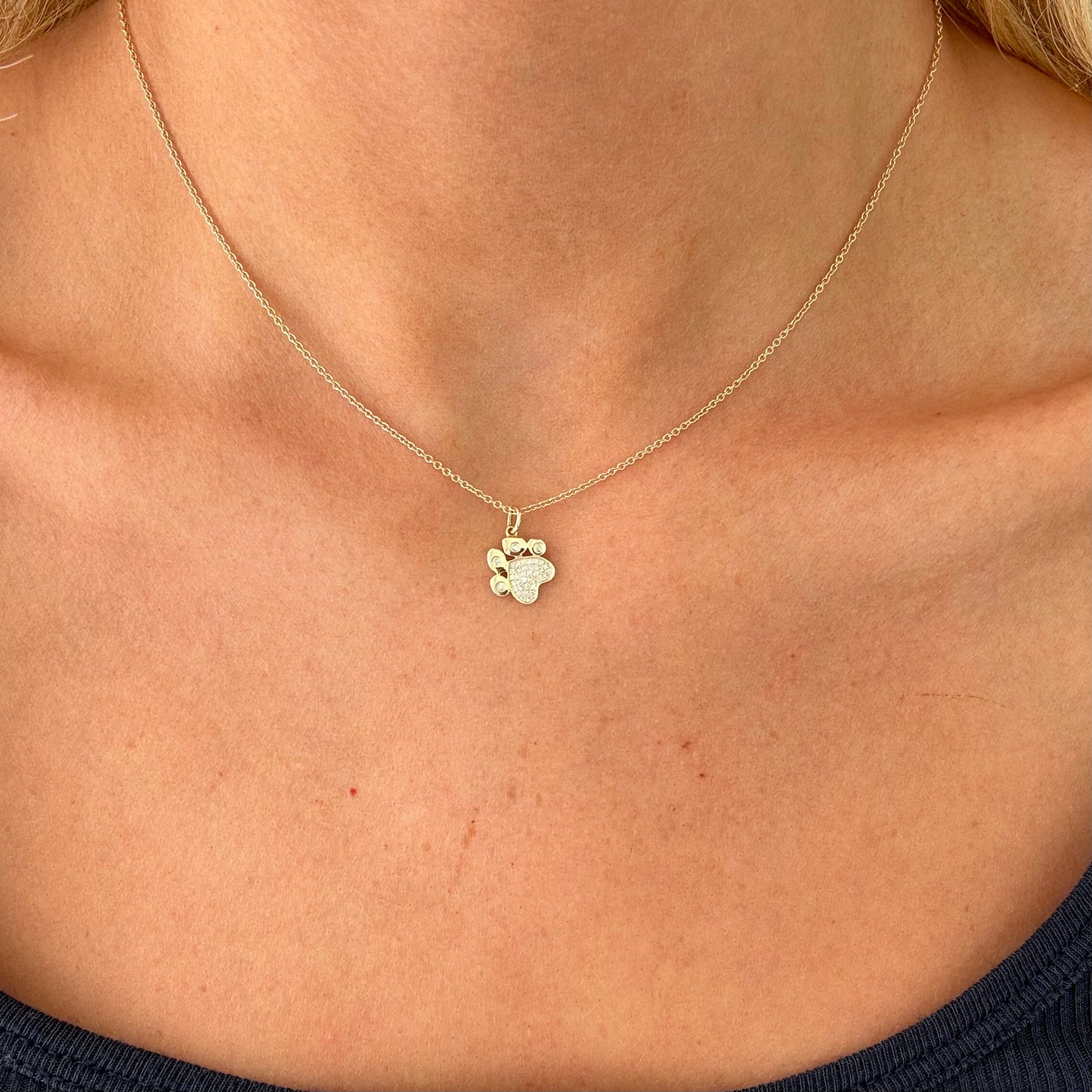 Close-up of a person's neck wearing the BEAR Gold Diamond Necklace by Dylan James Jewelry, featuring a pendant shaped like a clover. The person is dressed in a dark top.