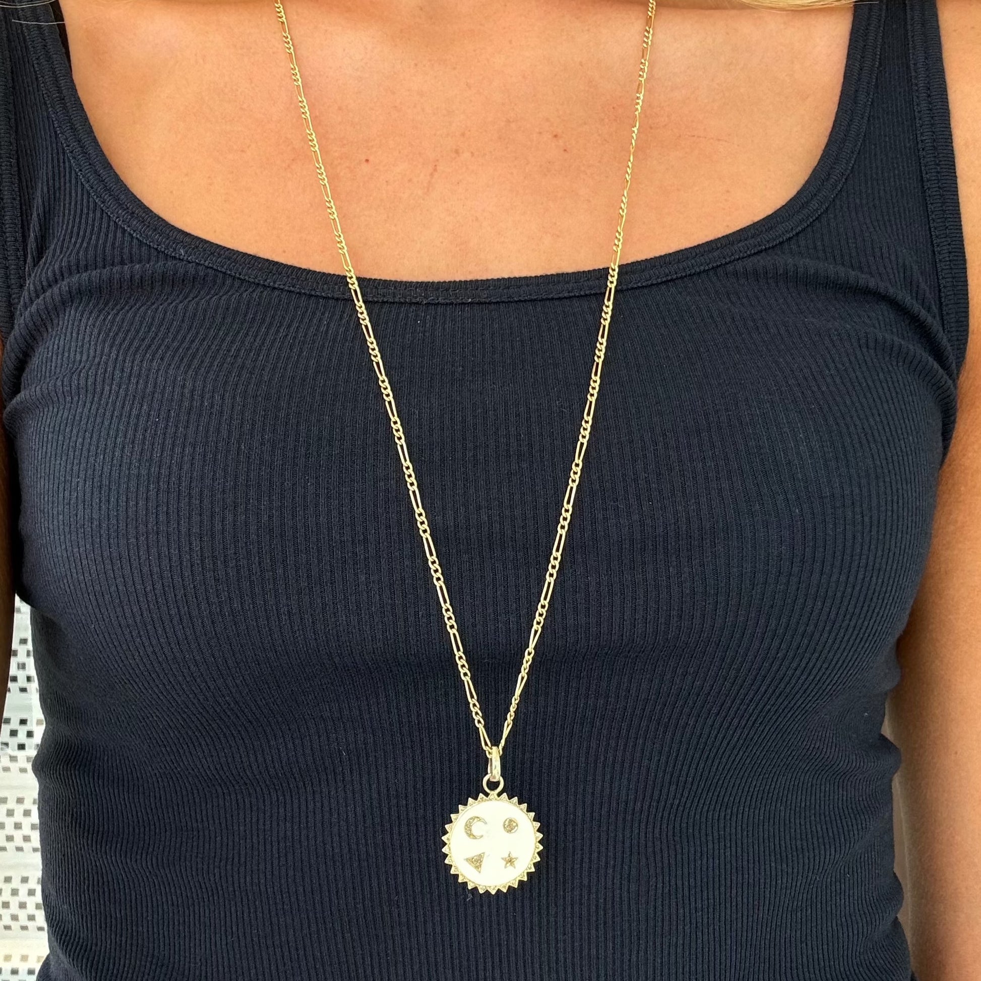 A person wearing a black sleeveless top and the Dylan James Jewelry STARR Enamel Necklace, which features a long gold-plated over silver chain with a circular pendant adorned with a crescent moon and star design.