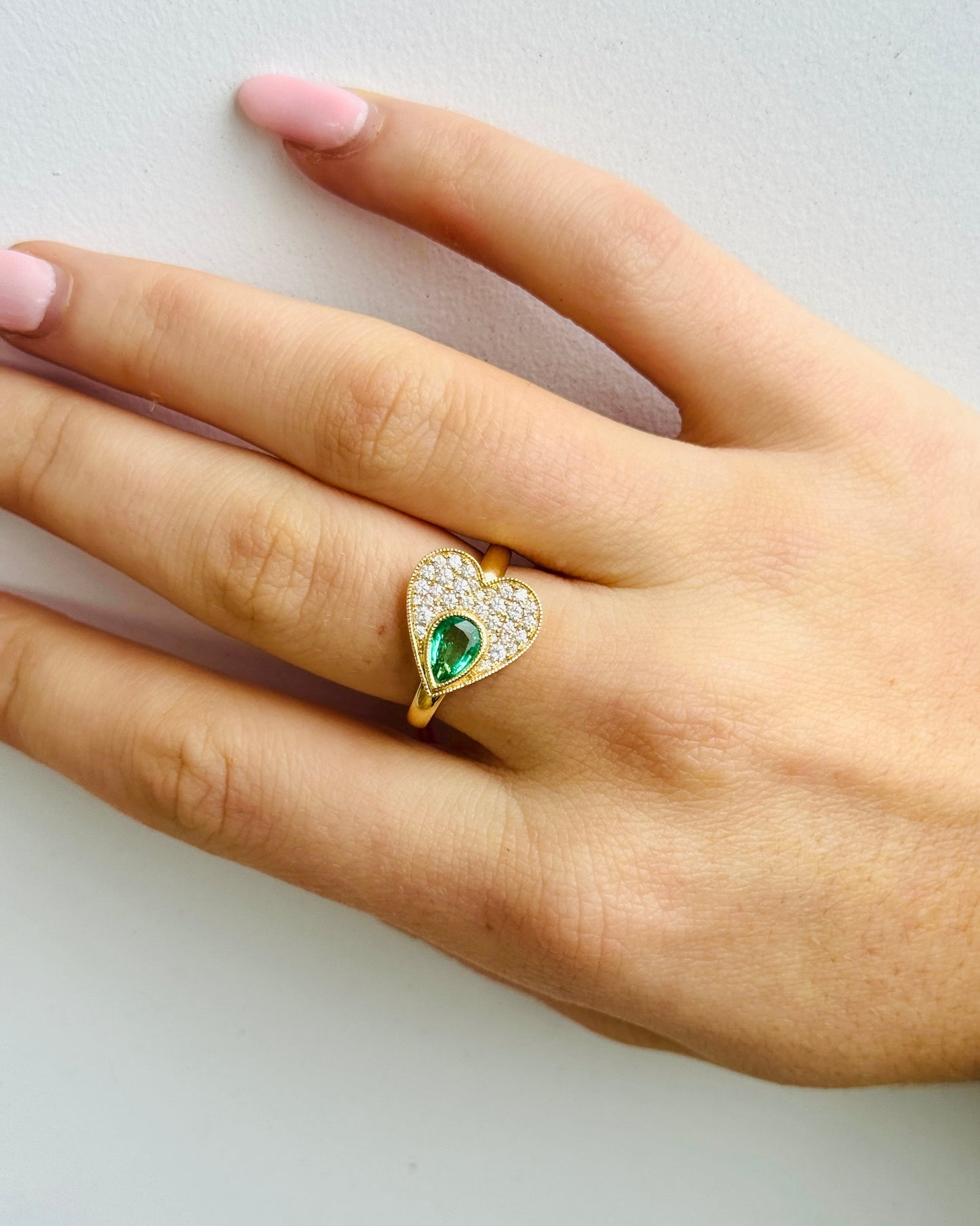 Hand wearing a gold ring with a green gemstone on a light background