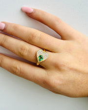 Hand wearing a gold ring with a green gemstone on a light background