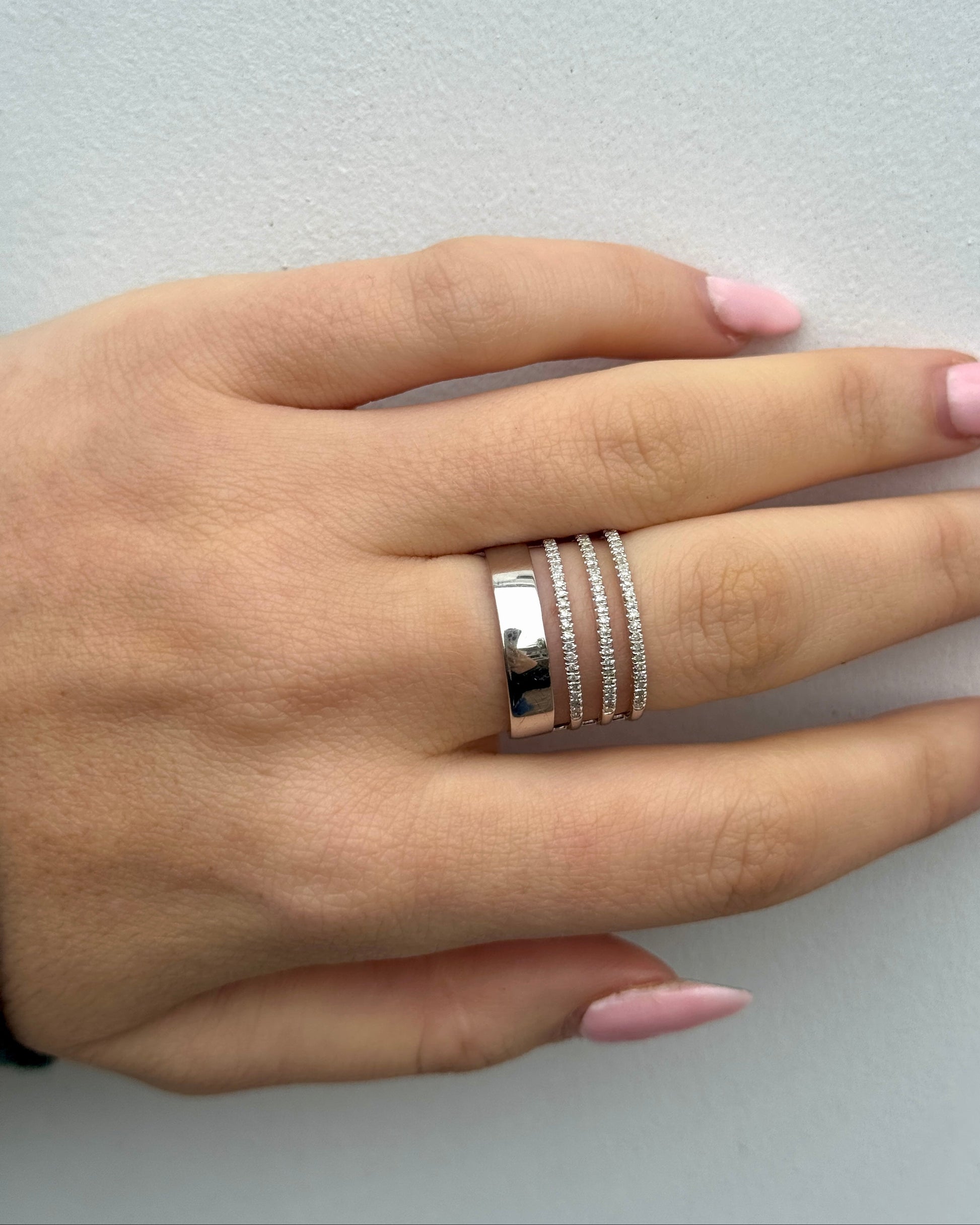 Hand wearing multiple rings on a light gray background