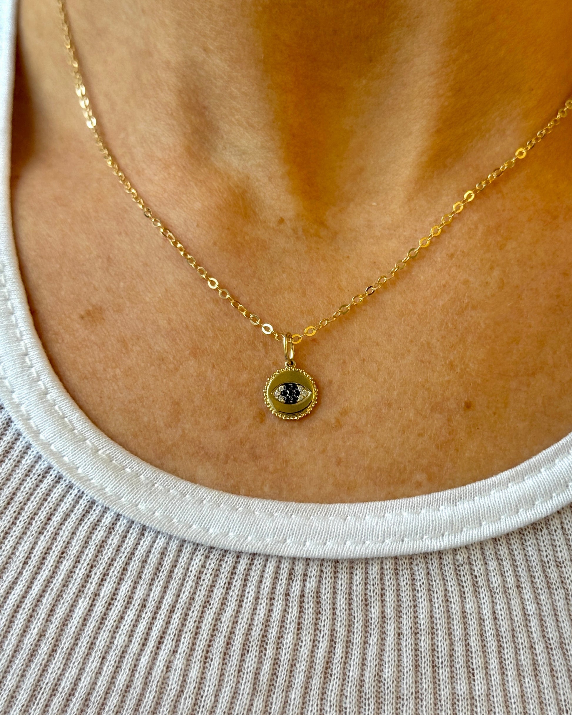 Gold necklace with a small pendant on a person wearing a white top.