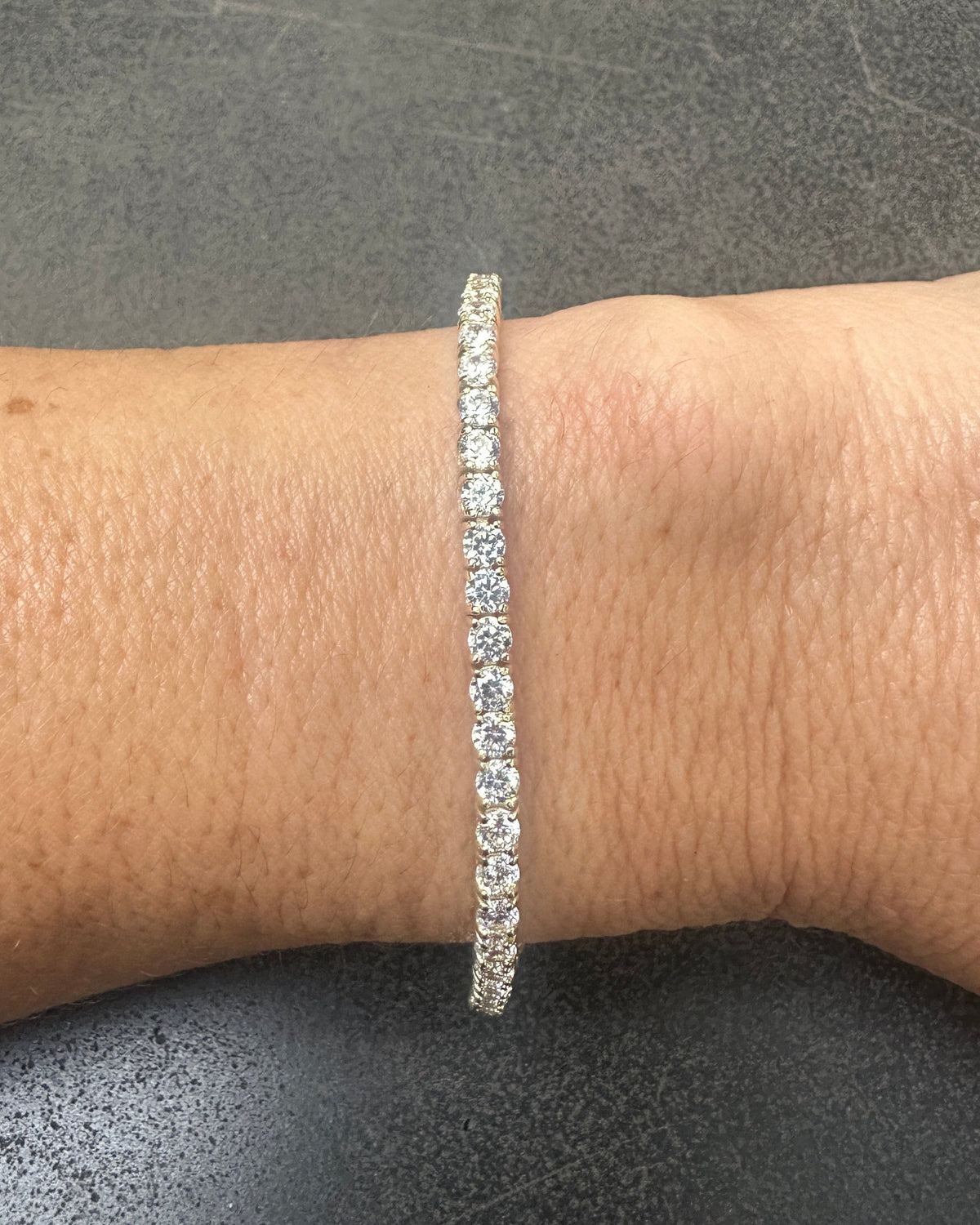 Close-up of a wrist adorned with the DANI Tennis Bracelet by dylan james jewelry, crafted from 925 Sterling Silver and Cubic Zirconia against a dark background.