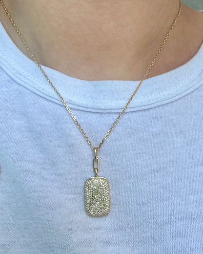 Gold necklace with a textured pendant worn by a person on a plain background