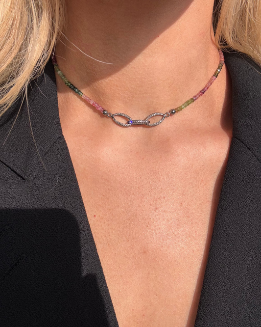 A person wearing the CLARA Silver Diamond Tourmaline Necklace by Dylan James Jewelry, featuring multicolor tourmaline beads and an infinity-shaped pendant, elegantly displayed against a black top.