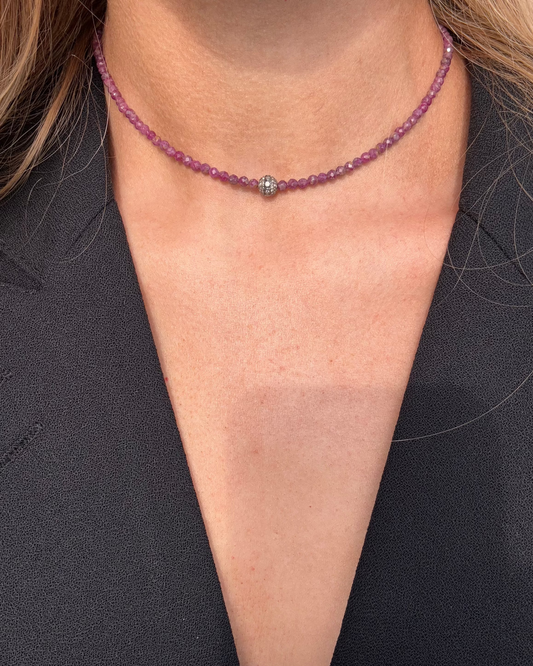 The ELLEN Diamond Ruby Necklace by Dylan James Jewelry elegantly graces the neck with a central sterling silver bead, its shimmer beautifully highlighted against a black fabric background.