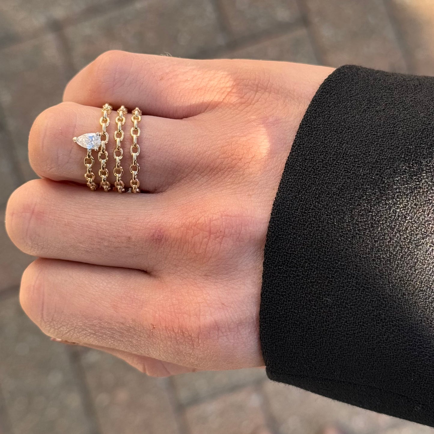 A hand in a black sleeve wears the LEE Gold Diamond Ring by AIRA, featuring a pear-shaped diamond set on three 14kt yellow gold chains.