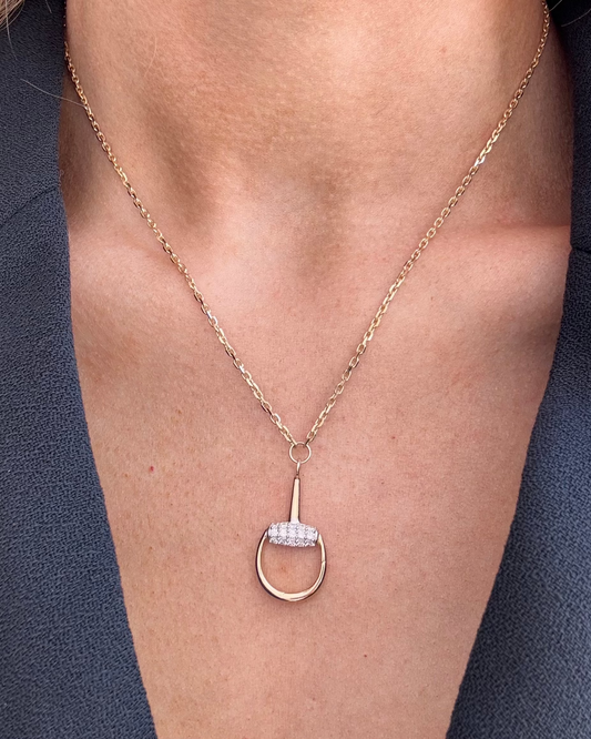 A person elegantly wears the AIRA BUD Gold Diamond Necklace, which features a yellow gold oval pendant with a small row of diamonds, paired with a dark blazer.