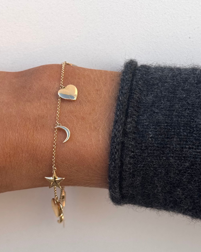 A wrist displays the ABBIE 14kt Charm Bracelet by Dylan James Jewelry, featuring charms of a heart, crescent moon, and star.