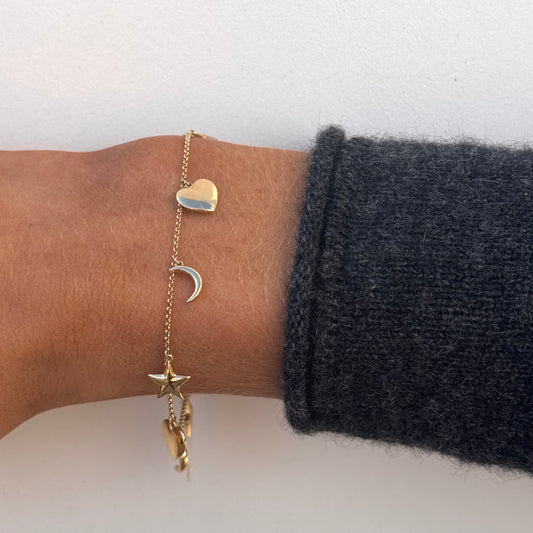 A wrist displays the ABBIE 14kt Charm Bracelet by Dylan James Jewelry, featuring charms of a heart, crescent moon, and star.