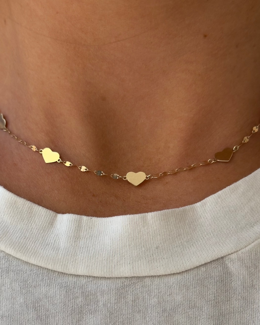 Close-up of the AMI Gold Necklace by Dylan James Jewelry, featuring heart-shaped 14kt yellow gold links, worn over a white shirt.