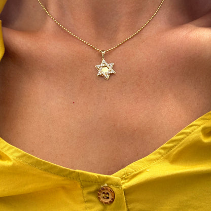 A person wearing a yellow shirt with one button visible and the Dylan James Jewelry KEBE Gold Diamond Star necklace on a ball chain of 14kt yellow gold.