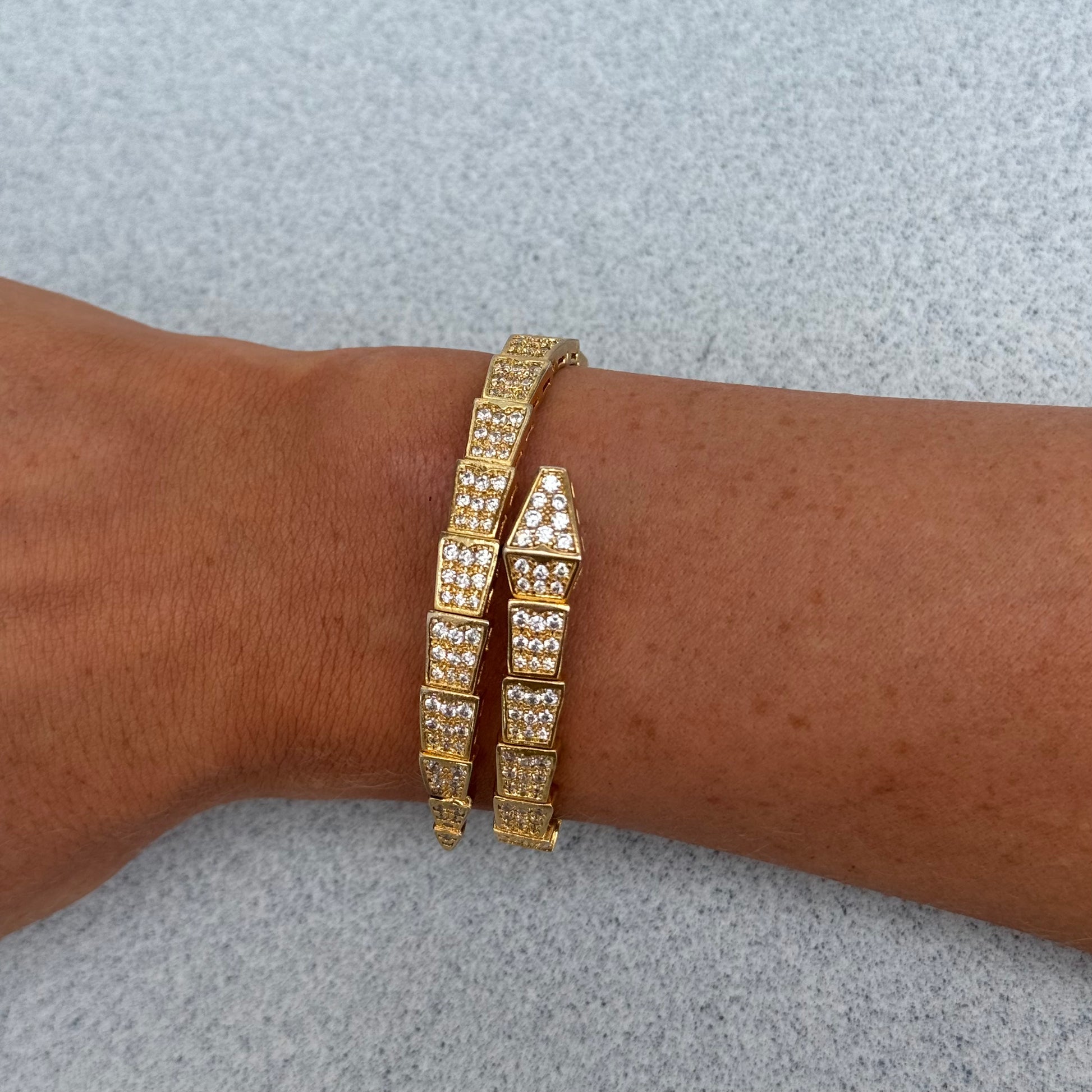 A wrist wearing the SNAKE Gold Diamond Bangle, a gold-plated brass bracelet from Dylan James Jewelry featuring multiple rectangular segments each adorned with small cubic zirconia stones, against a light gray background.