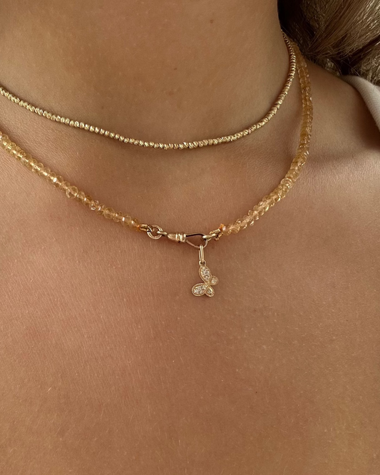 Close-up of a person's neck wearing two necklaces: a delicate 14kt yellow gold chain and the Dylan James CITRINE Beaded Butterfly Necklace featuring a small gold butterfly charm.