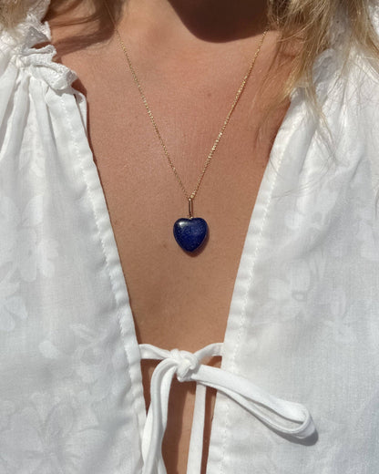 Person wearing a white blouse with a blue heart pendant necklace.