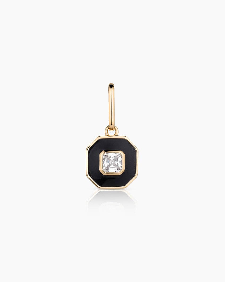Gold charm with a black enameled setting and clear gemstone on a white background