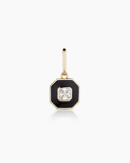 Gold charm with a black enameled setting and clear gemstone on a white background