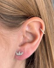 Close-up of an ear wearing a gold hoop in the cartilage and a silver leaf earring in the lobe, beautifully enhanced by Dylanjmaes' KAI Diamond Earrings featuring a 14K white gold lotus flower design.