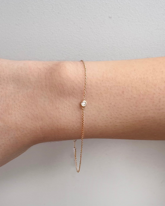 Close-up of an arm wearing the AILYNN Diamond Bracelet by Dylan James Jewelry, featuring a minimalist 14kt gold chain with a small round diamond gem on a light background.